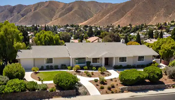 A wide view of a San Fernando Valley home with a light colored shingle roof under bright afternoon sun